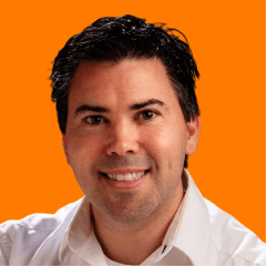 Blake Cohlan smiling, with dark hair and wearing a white shirt against an orange background.