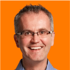 Julian Foster, wearing glasses and with short hair against an orange background, dons a blue striped shirt, exuding a friendly vibe.